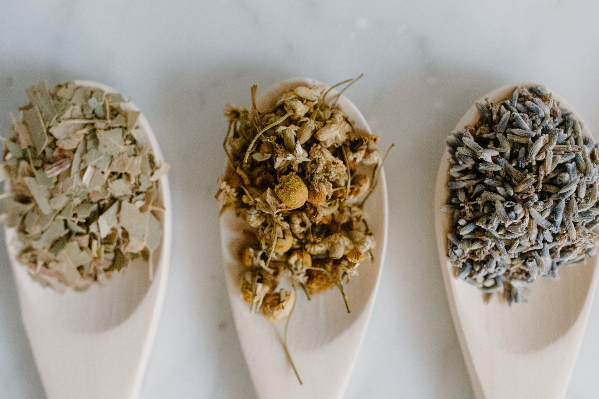 Three wooden spoons filled with dried herbs on a table.