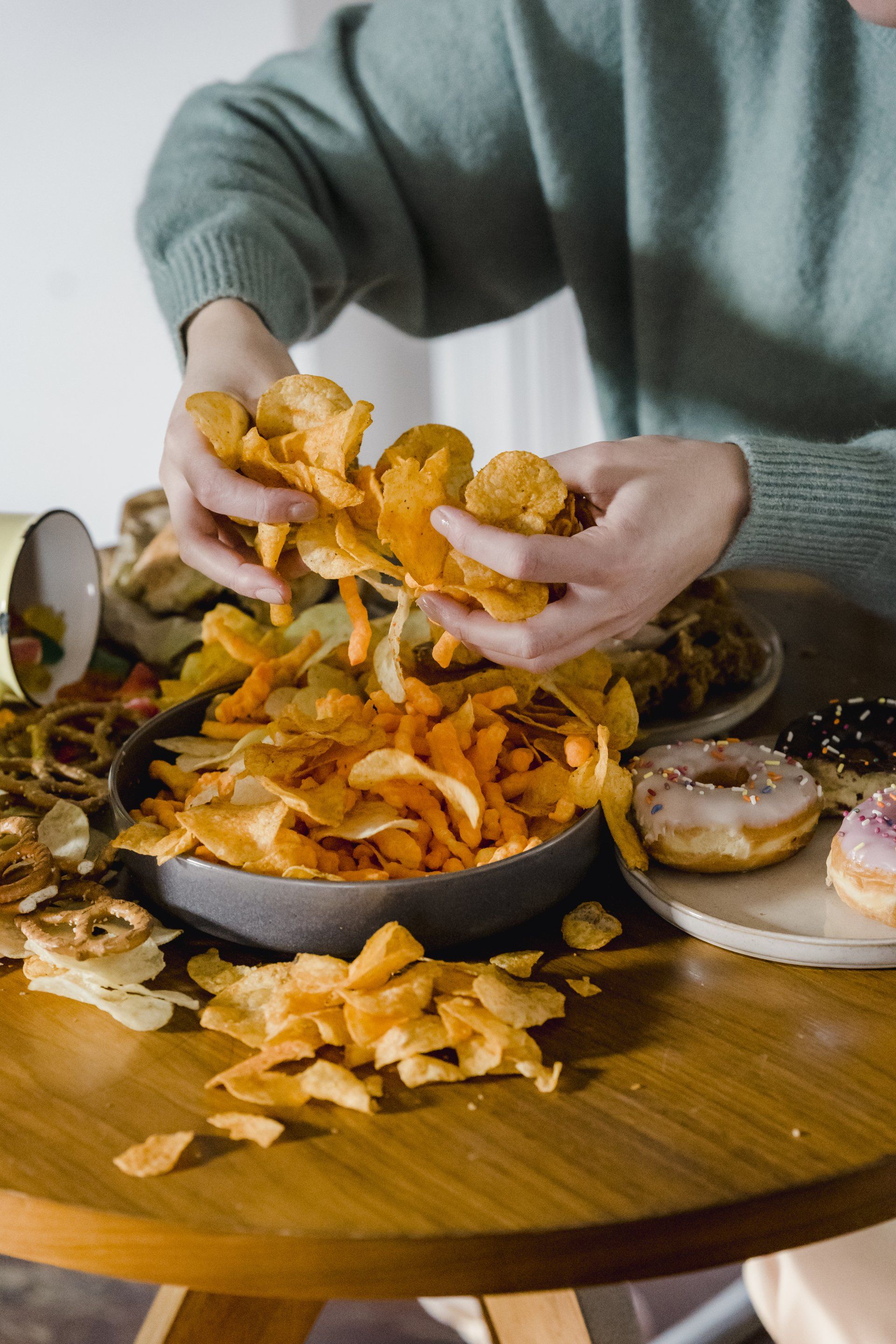 A person is sitting at a table eating chips and donuts.