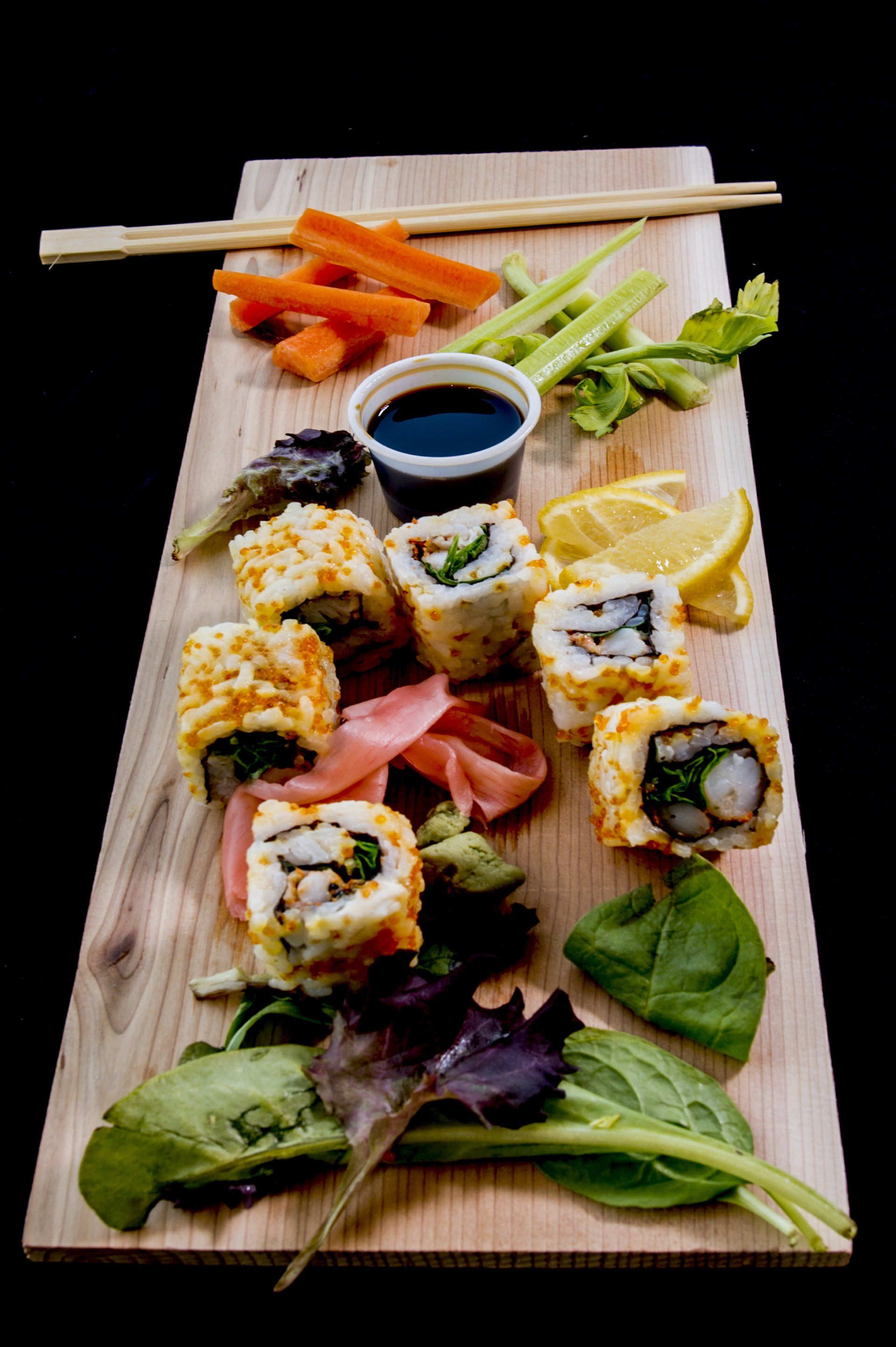 A wooden cutting board topped with sushi and vegetables