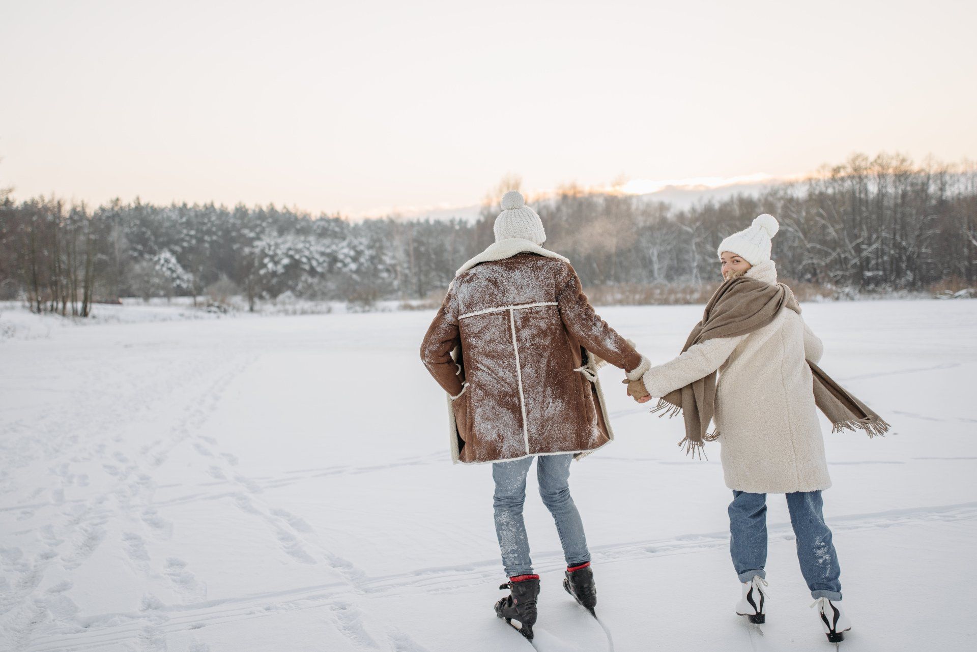 A man and a woman are holding hands while ice skating on a frozen lake.