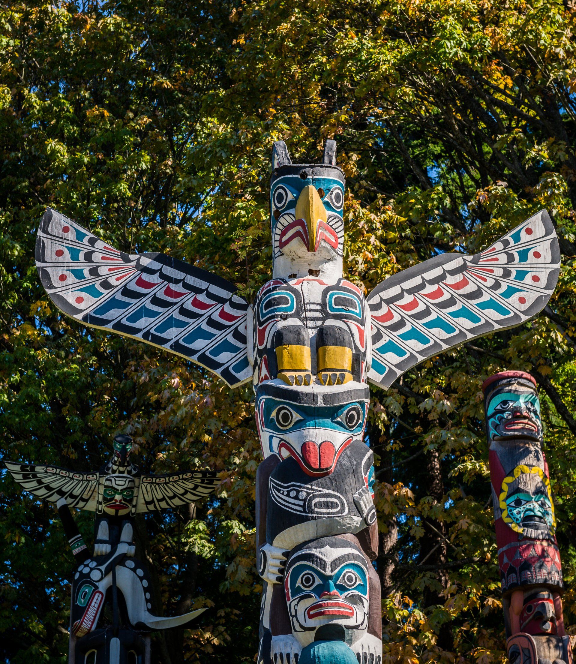 A totem pole with a bird on top of it is surrounded by trees.