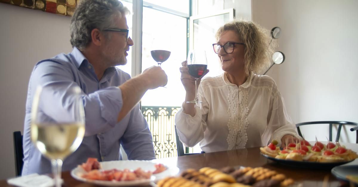 A man and a woman are sitting at a table toasting with wine glasses.