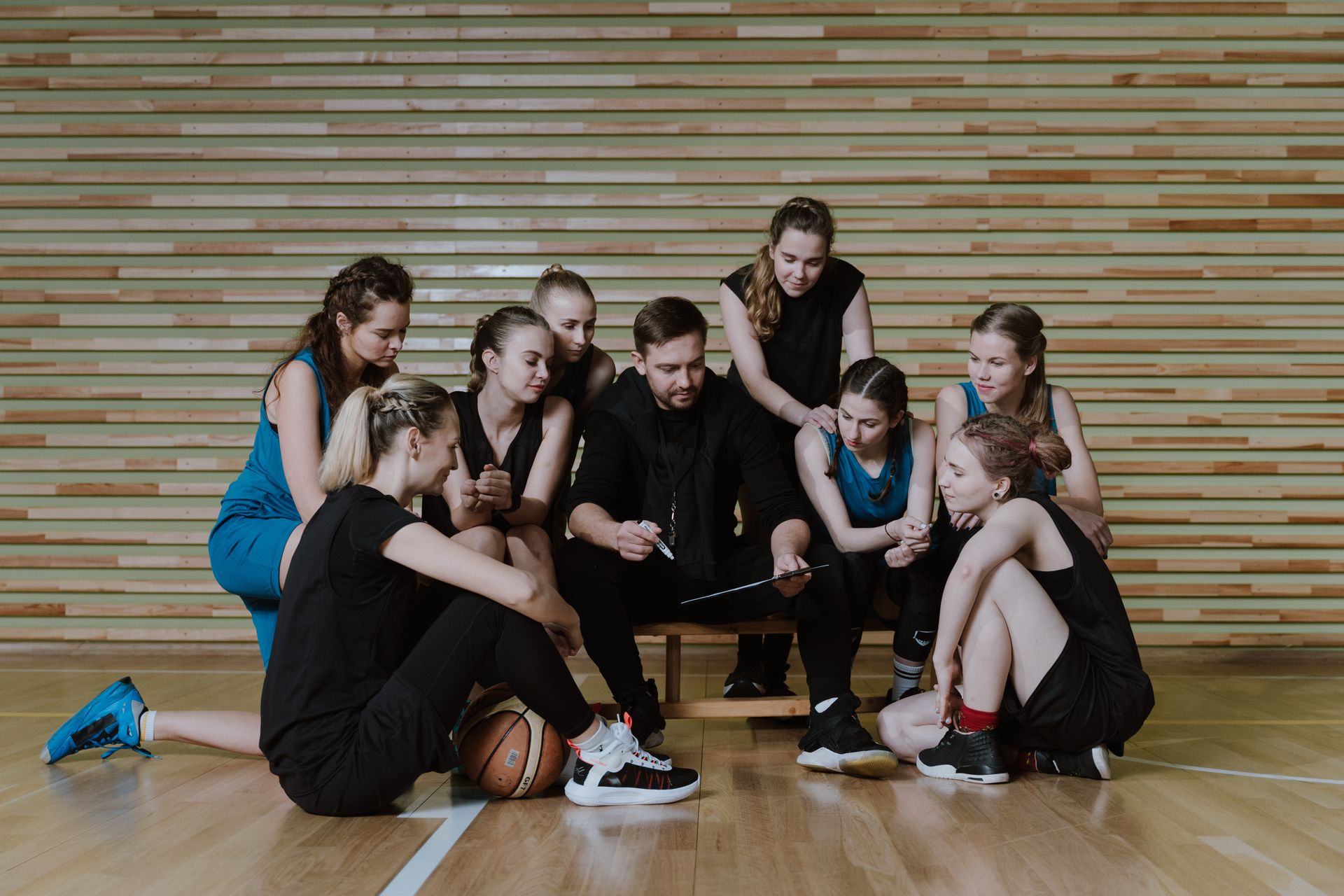 A group of female basketball players are sitting on the floor with their coach.