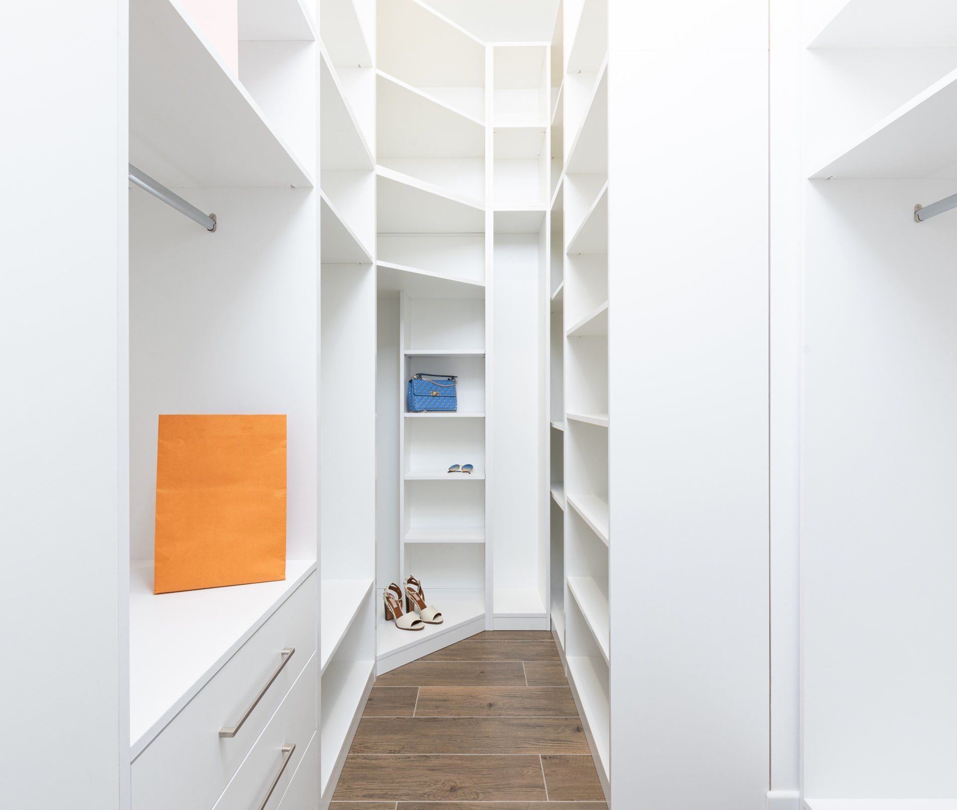 A walk in closet with white shelves and a wooden floor.