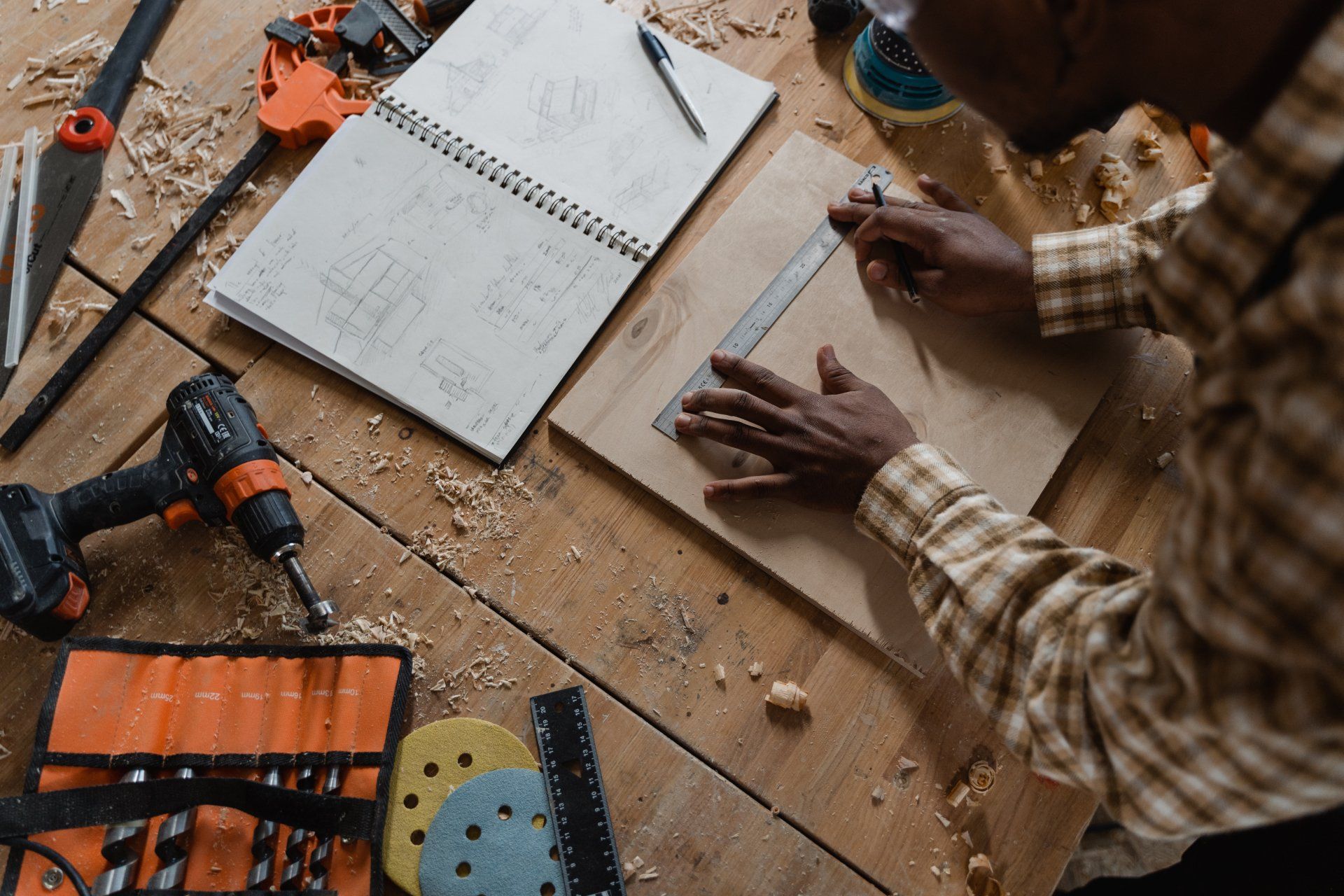 A man is sitting at a wooden table working on a piece of wood.