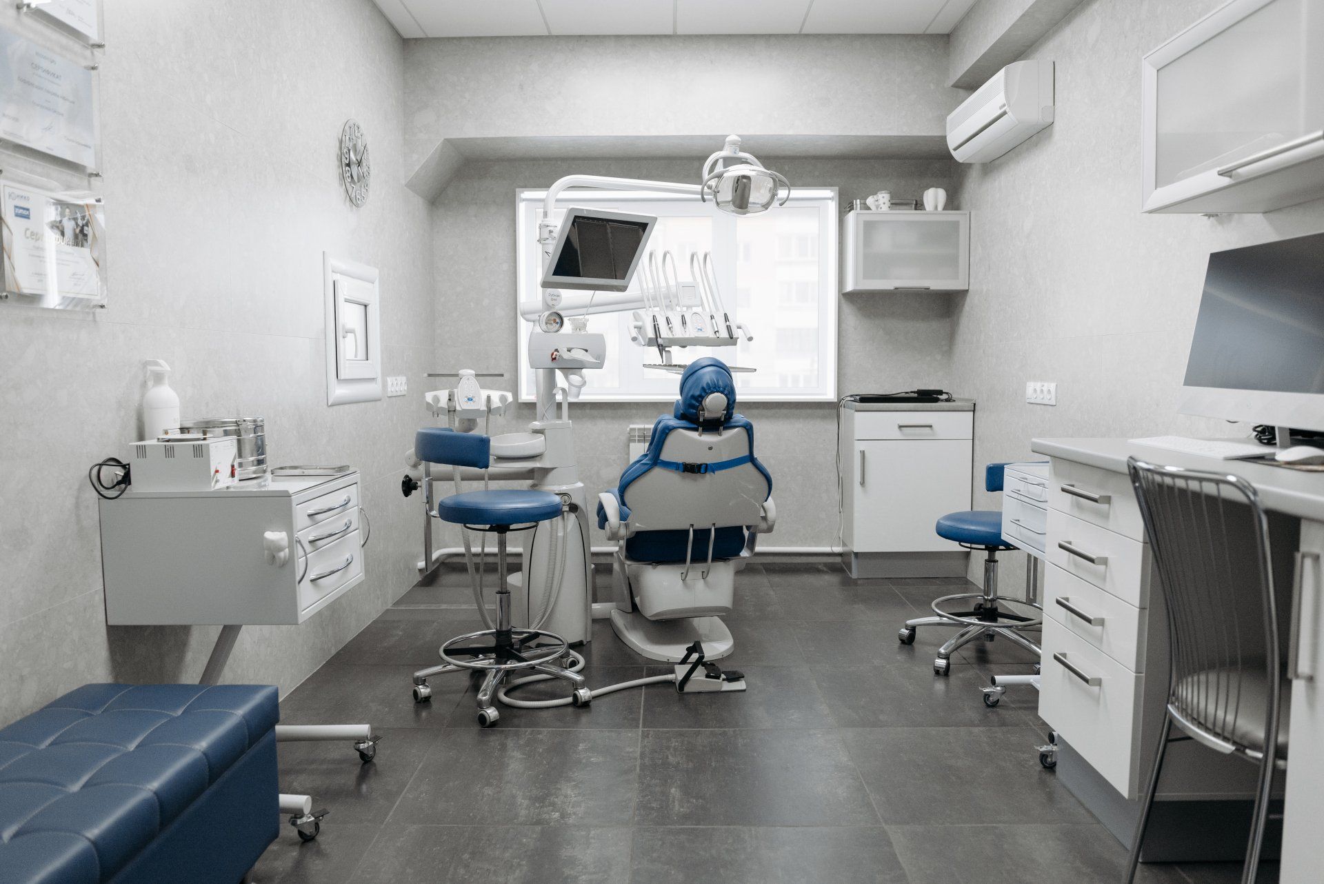 Dental office with a chair, equipment, and cabinets. White walls, blue accents, and gray floor.