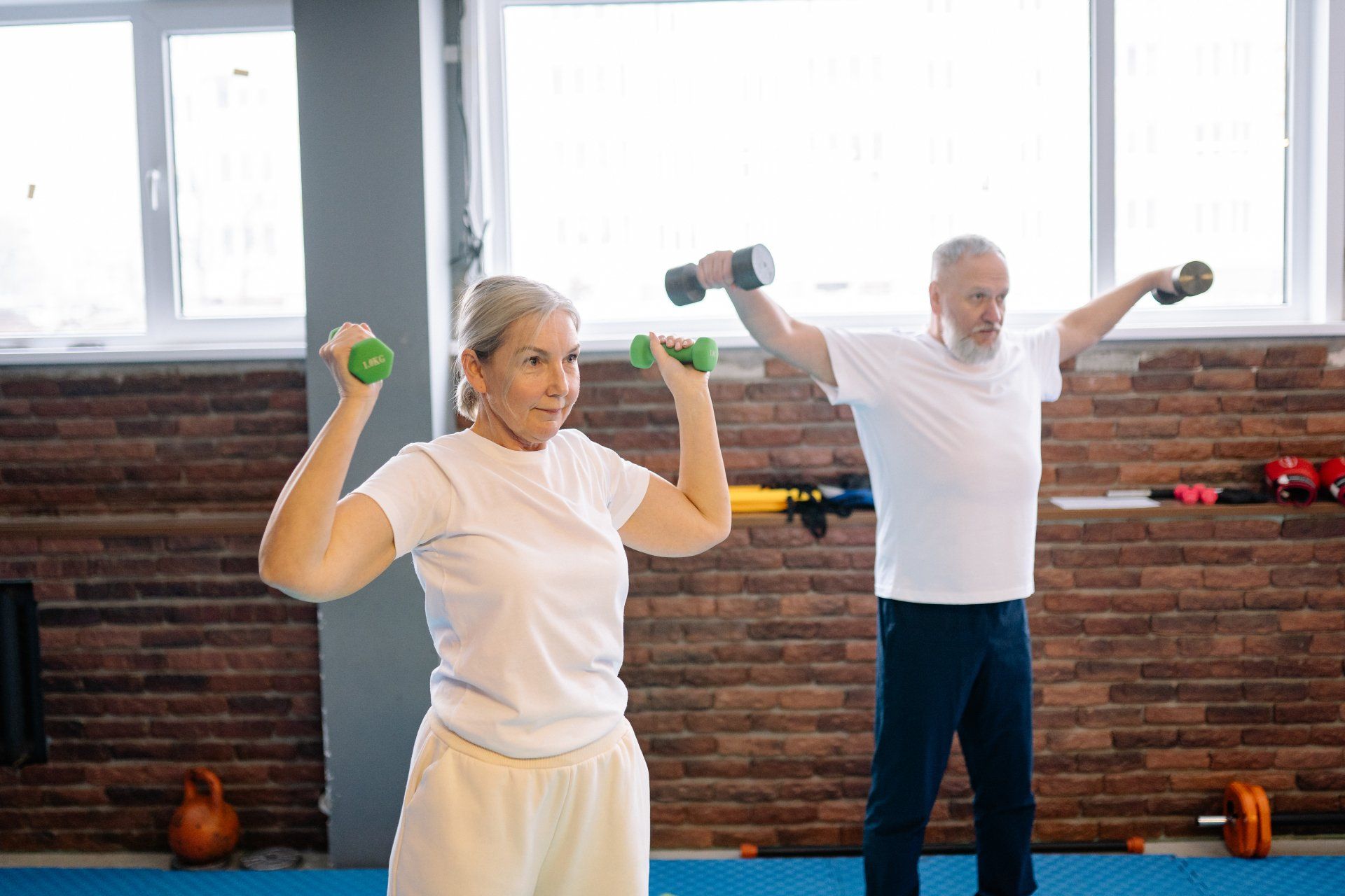 A man and a woman are lifting dumbbells in a gym.