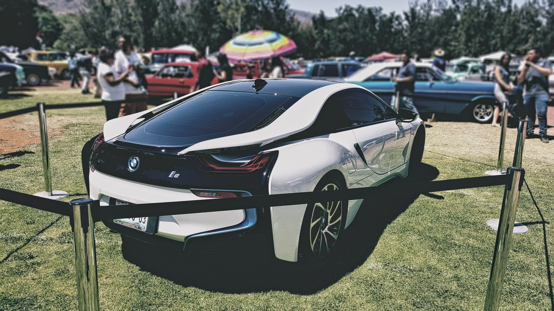 A white bmw i8 is parked in a grassy field at a car show.