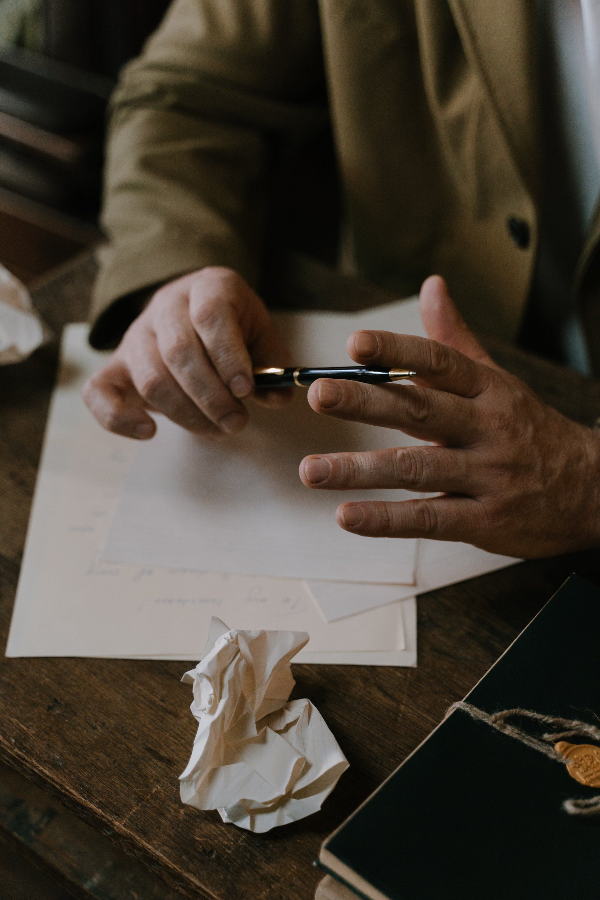 A man is sitting at a table holding a pen and writing on a piece of paper.