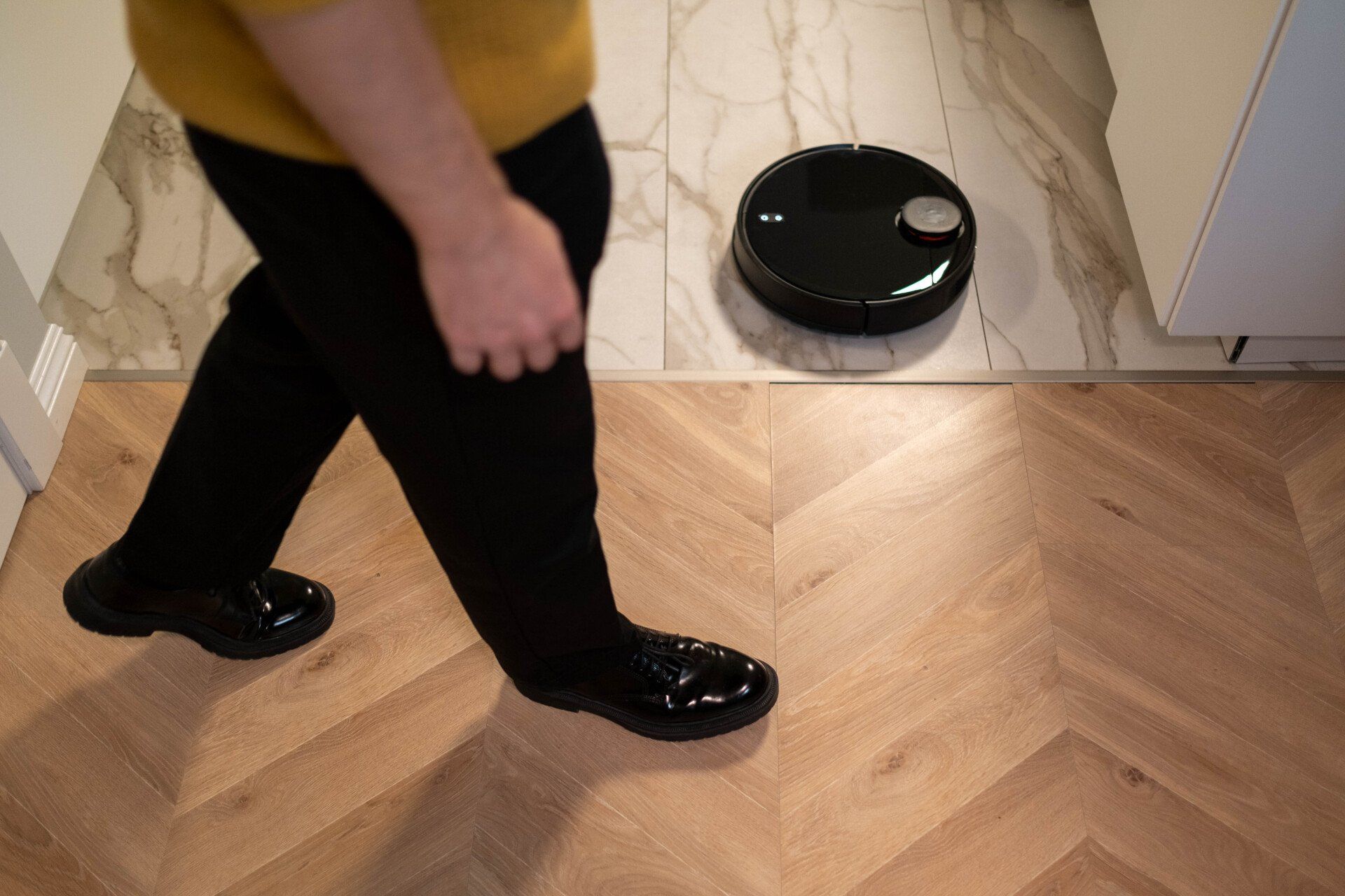 A person is walking next to a robot vacuum cleaner on a wooden floor.