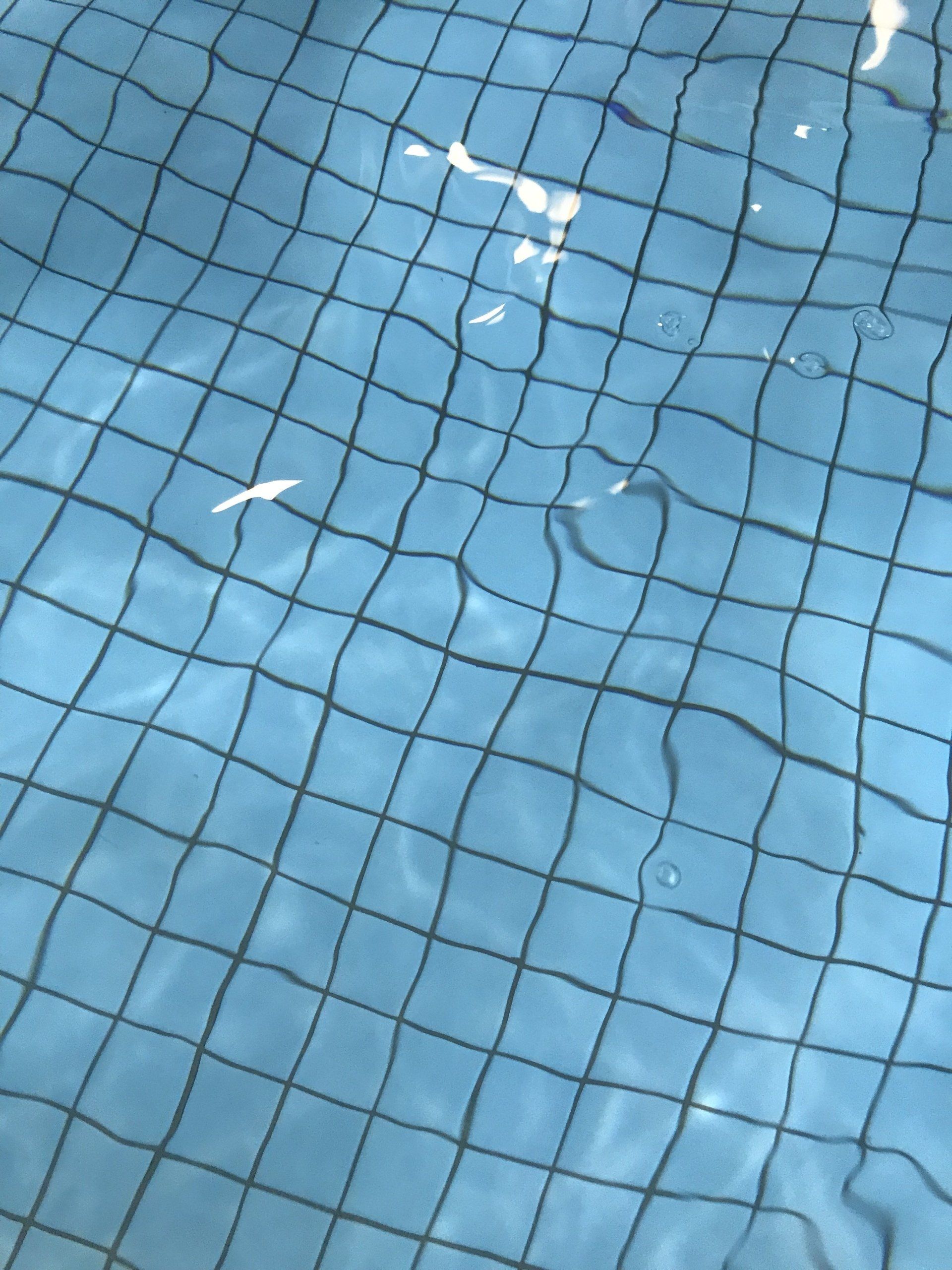 Clear blue pool water reflecting light with a square tile pattern on the bottom of the pool
