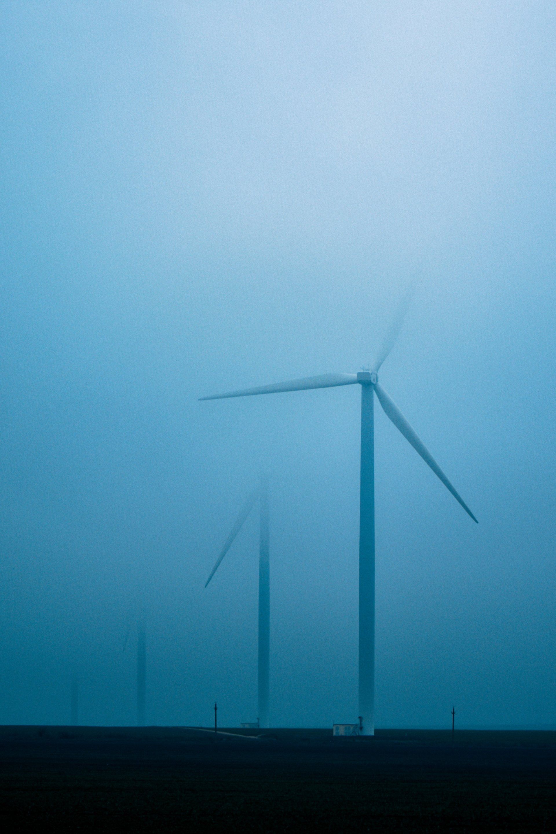 a row of wind turbines in the fog against a blue sky in Glasgow.