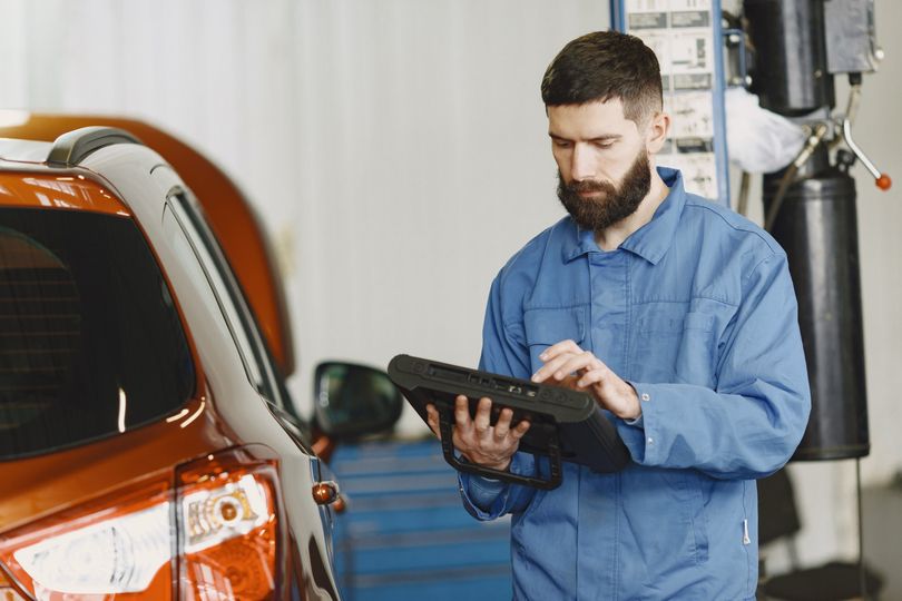 a man is using a tablet in a garage next to a car .