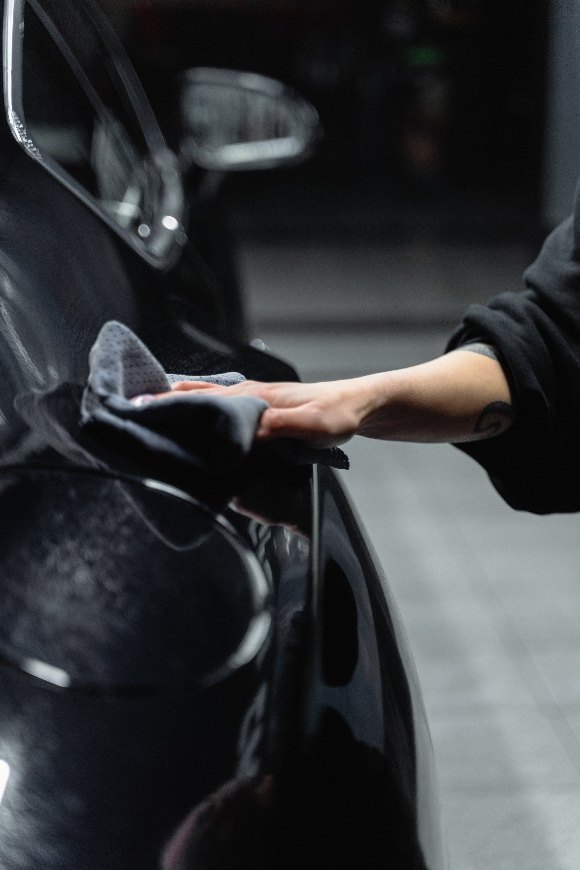 a person is cleaning a black car with a cloth.