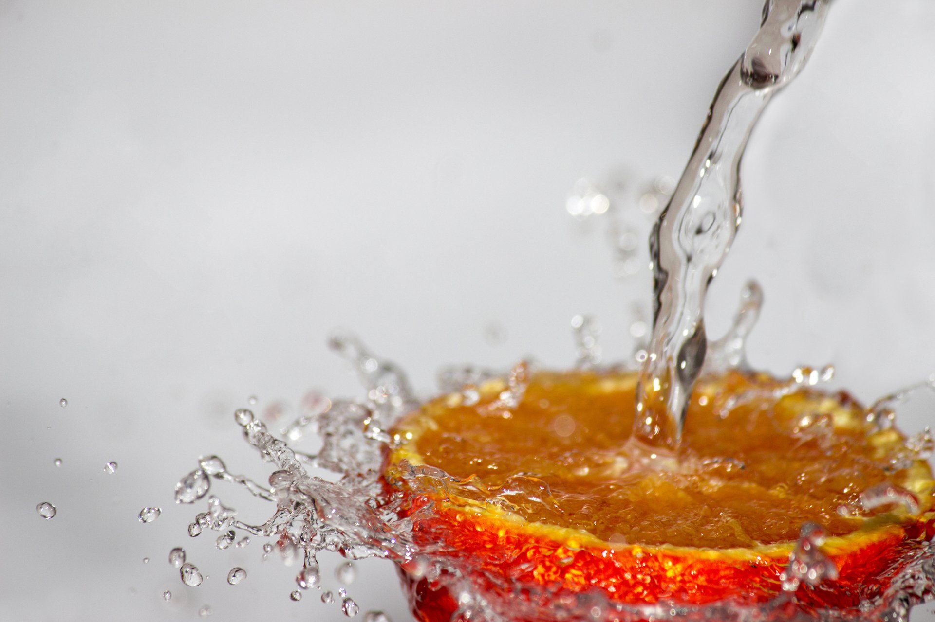 A slice of orange is being splashed with water.