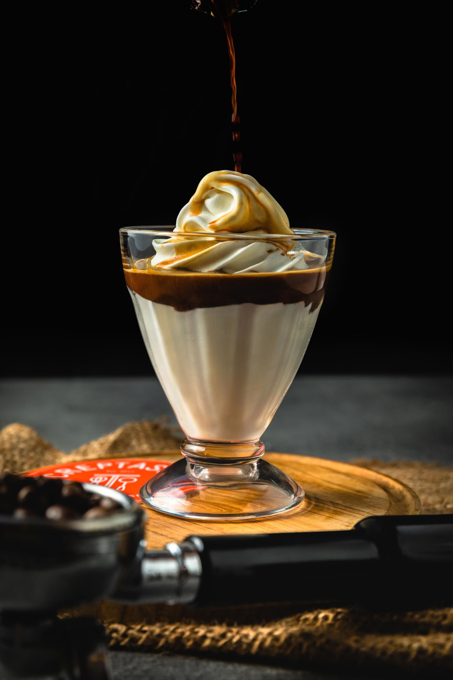 A glass of ice cream with whipped cream and coffee being poured into it.