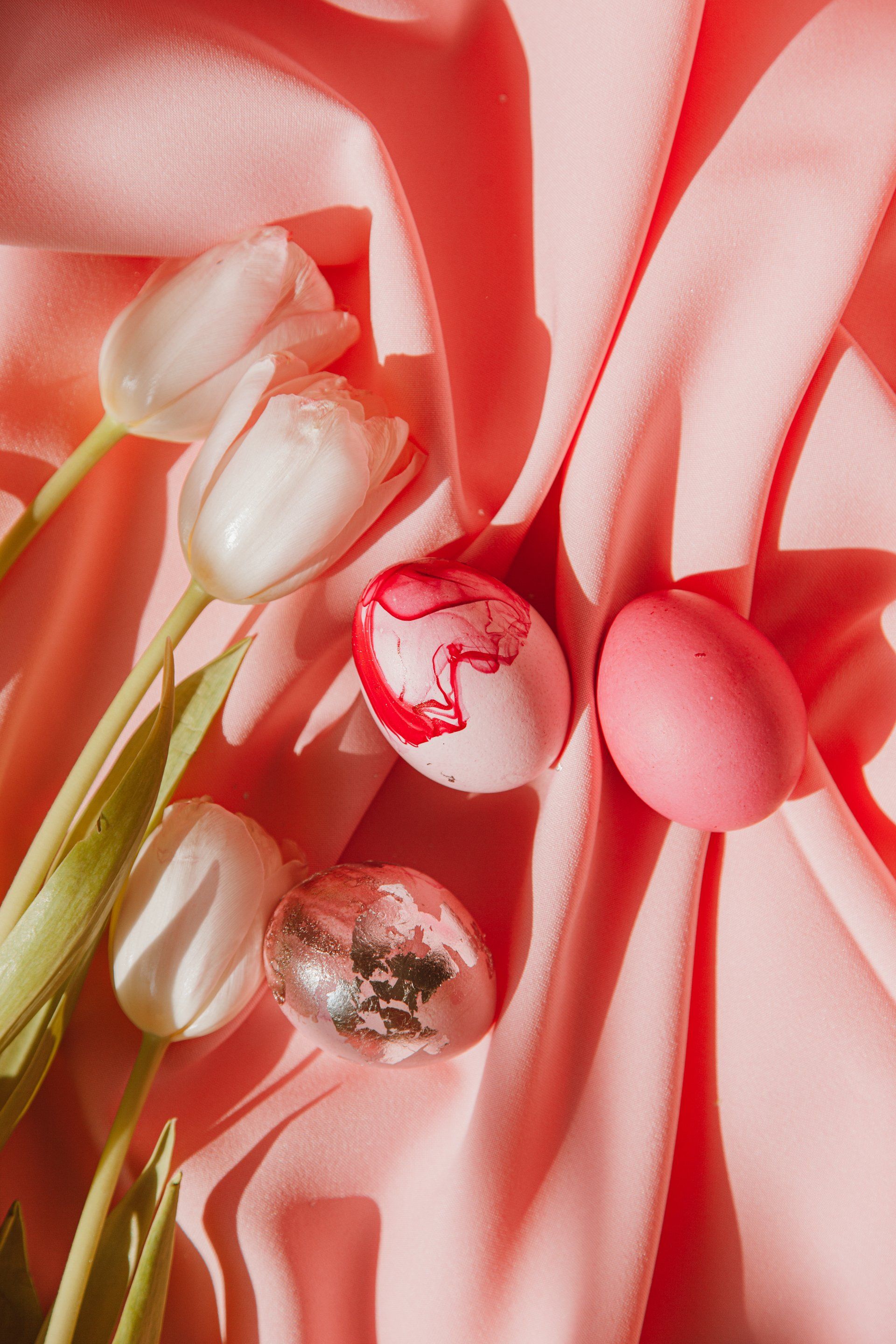 ein Strauß weißer Tulpen und rosa Ostereier auf einem rosa Tuch.