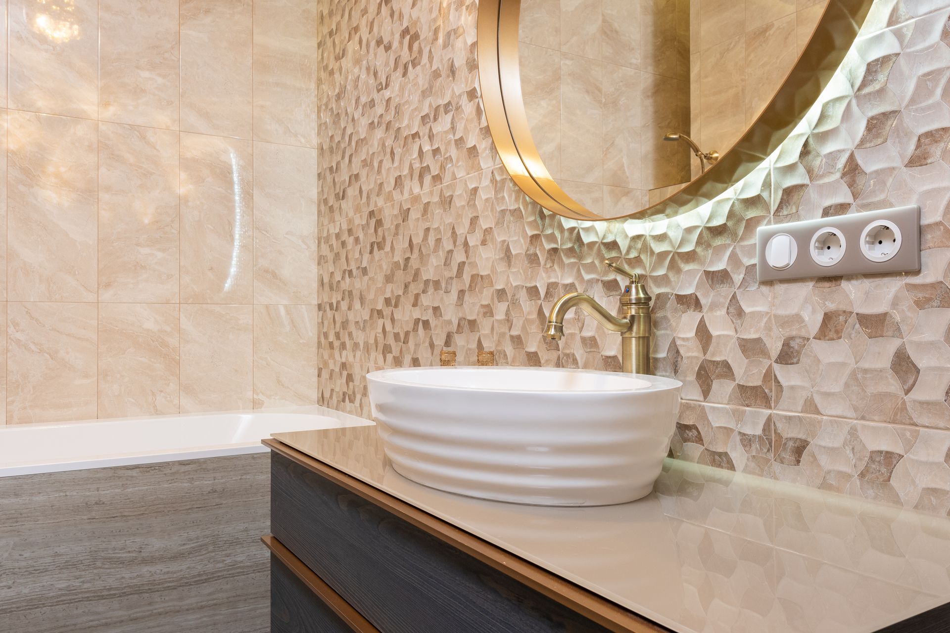 A stand alone sink with a gold faucet sits in front of a geometric tile accent wall