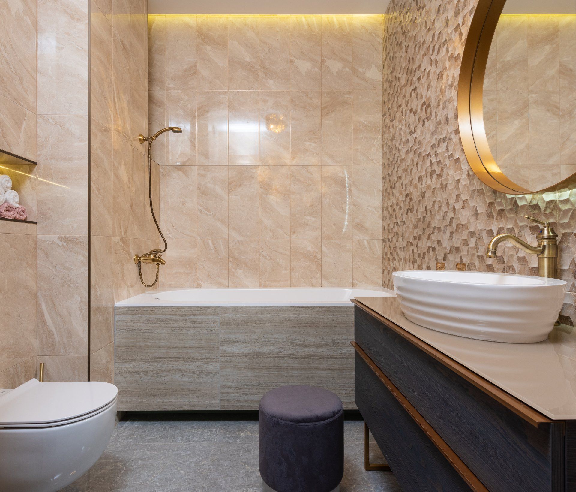 A gold themed bathroom with beautiful tan marbled walls and an accent wall with geometric shapes.