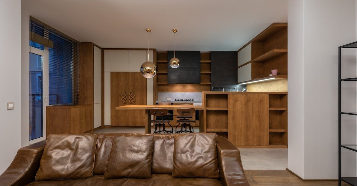 A living room with a brown leather couch and a kitchen in the background.