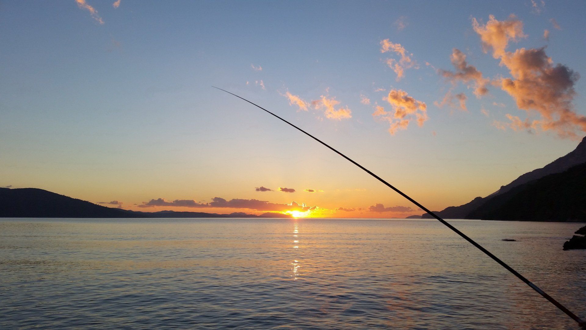 A person is fishing in the ocean at sunset