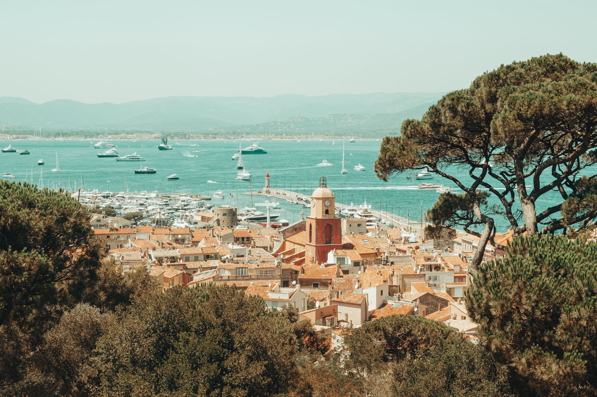Une ville côtière avec des bâtiments aux toits rouges, un port rempli de bateaux et une tour de l'horloge.