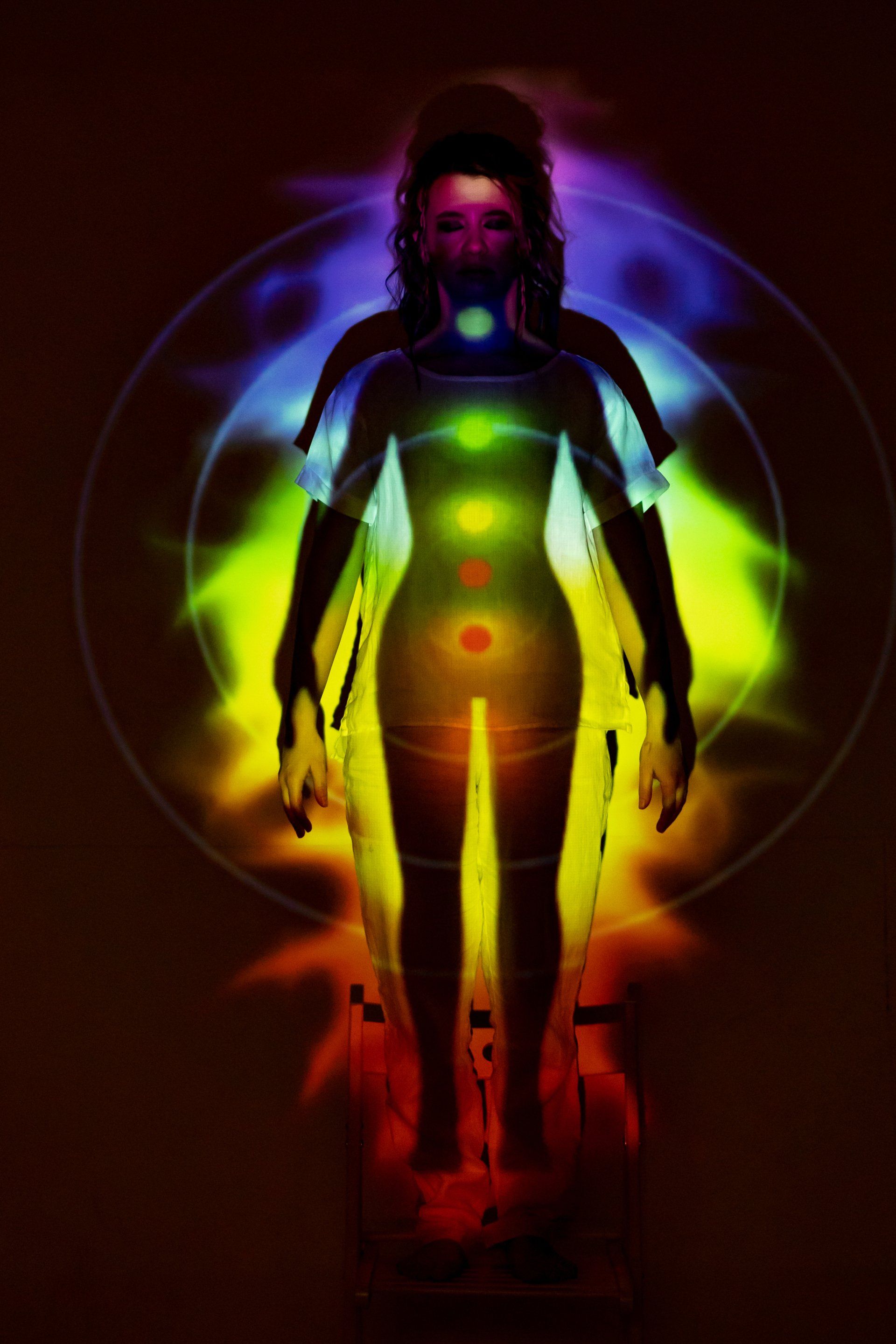 A woman is standing in front of a rainbow of chakras.