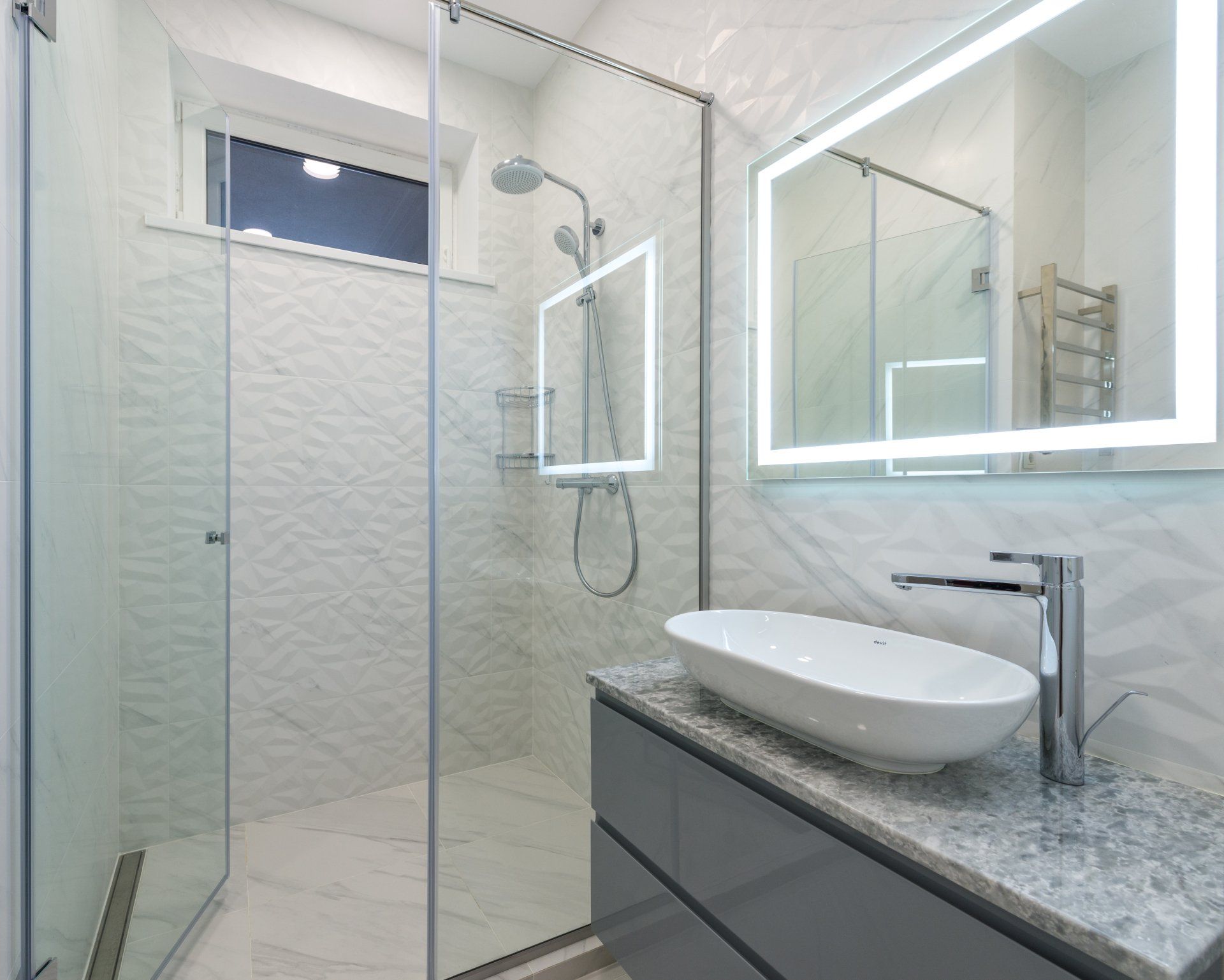 Bright bathroom with granite countertop and white geometric tile shower walls.