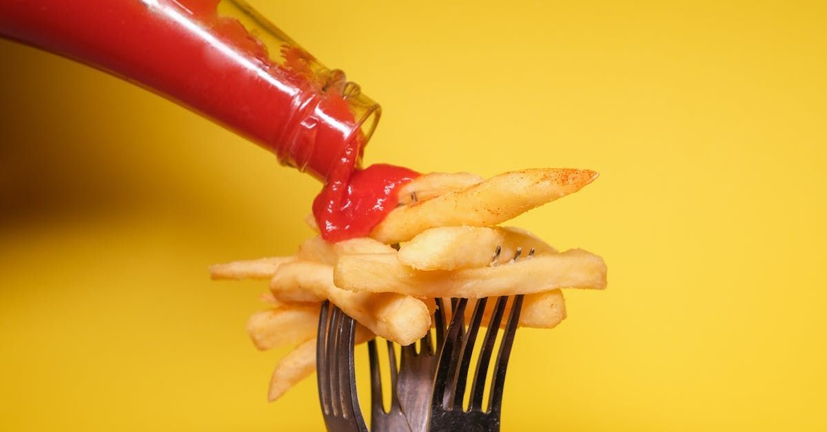Ketchup is being poured on french fries on a fork.