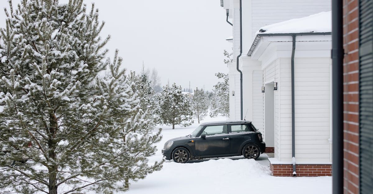 A car is parked in the snow in front of a house.