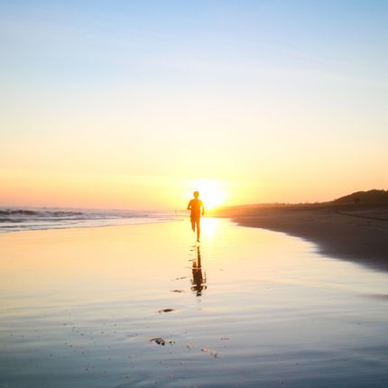 A person is running on the beach at sunset.