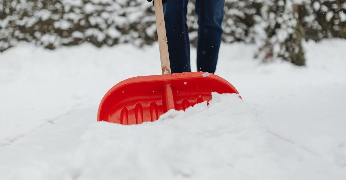 A person is shoveling snow with a red shovel.