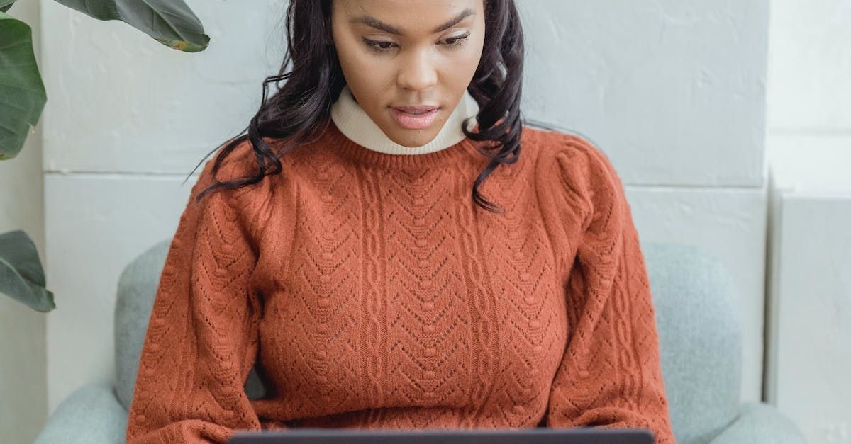 A woman in an orange sweater is sitting in a chair using a tablet computer.