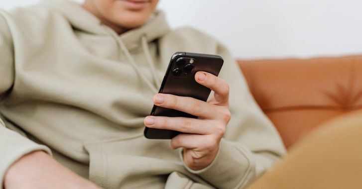 A man is sitting on a couch using a cell phone.