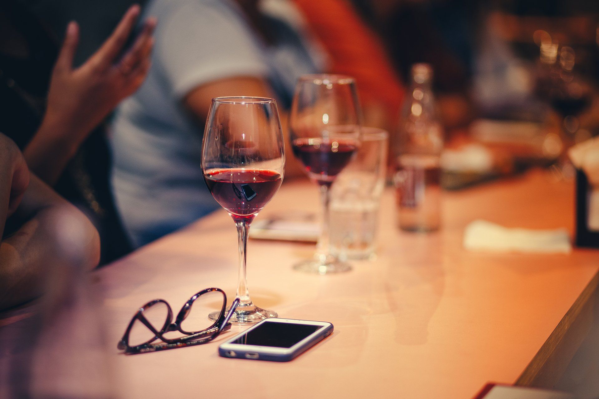 2 glasses of red wine, glasses and a phone sitting on a bar
