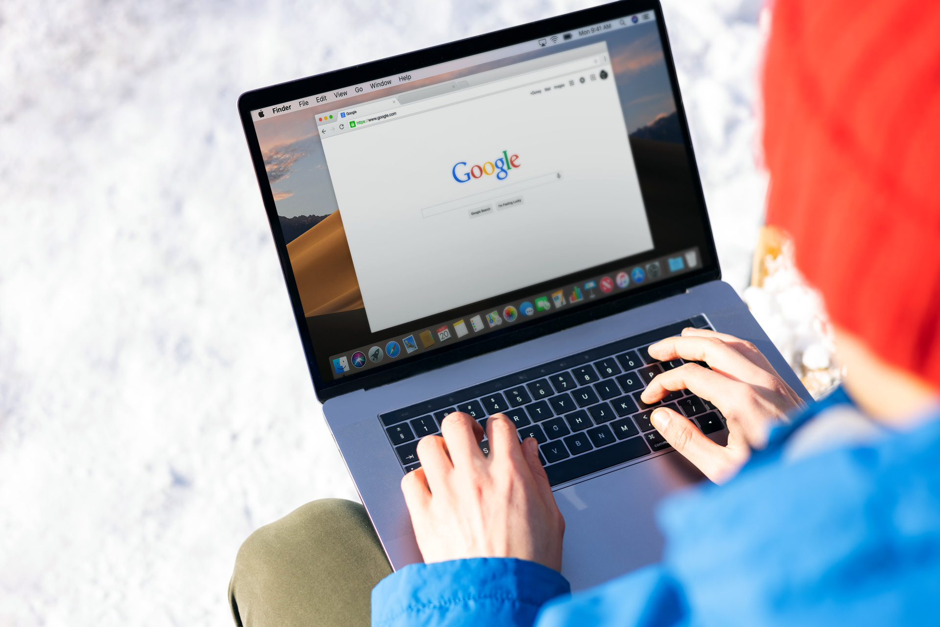 a person is typing on a laptop computer while sitting in the snow .