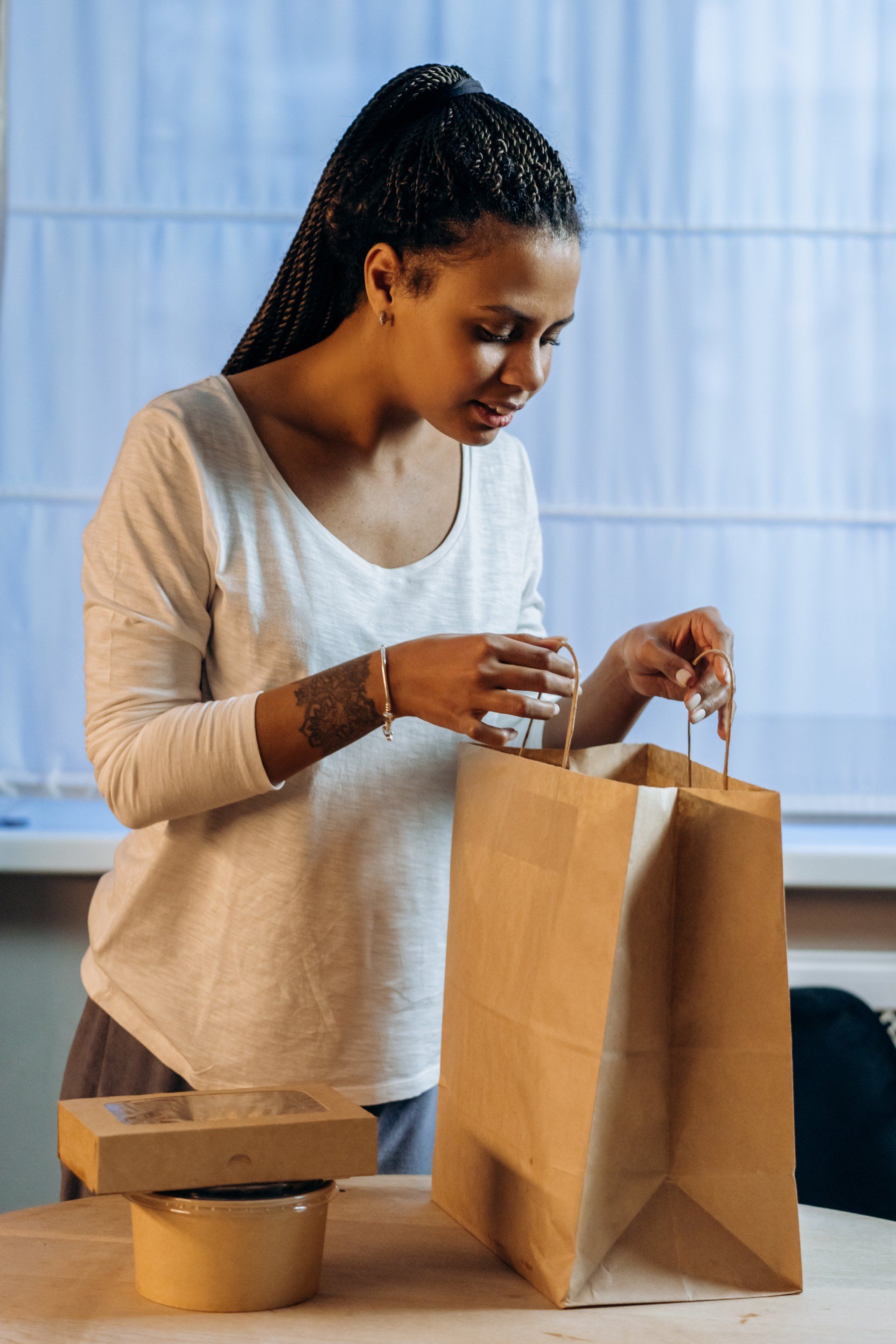 A woman is sitting at a table holding a brown paper bag.