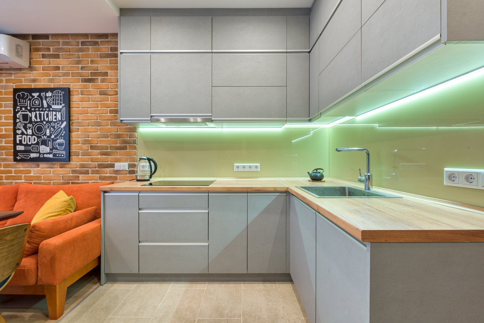 A kitchen with a sink , cabinets , a couch and a brick wall.