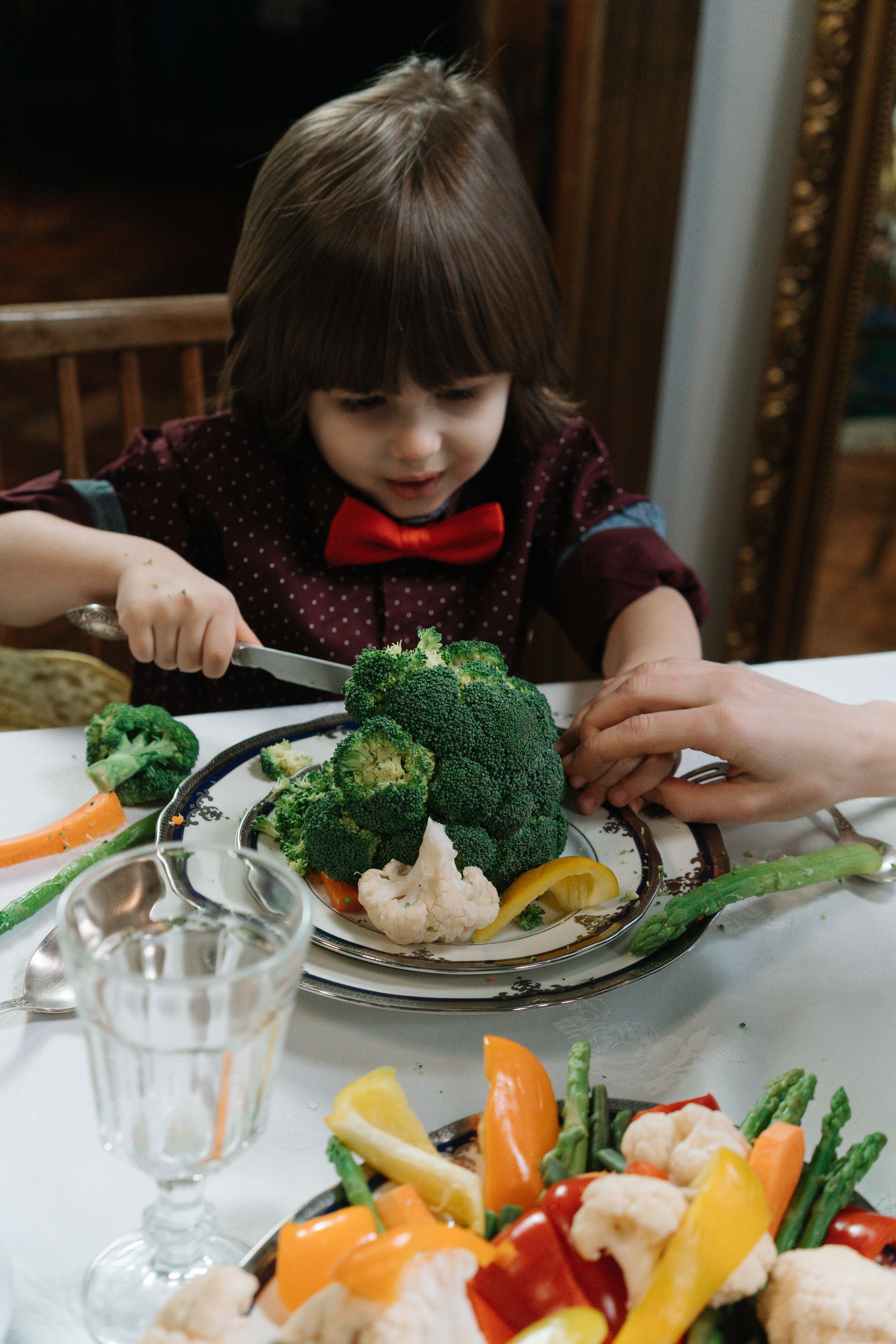 A kid cutting broccoli on a plate at a table.