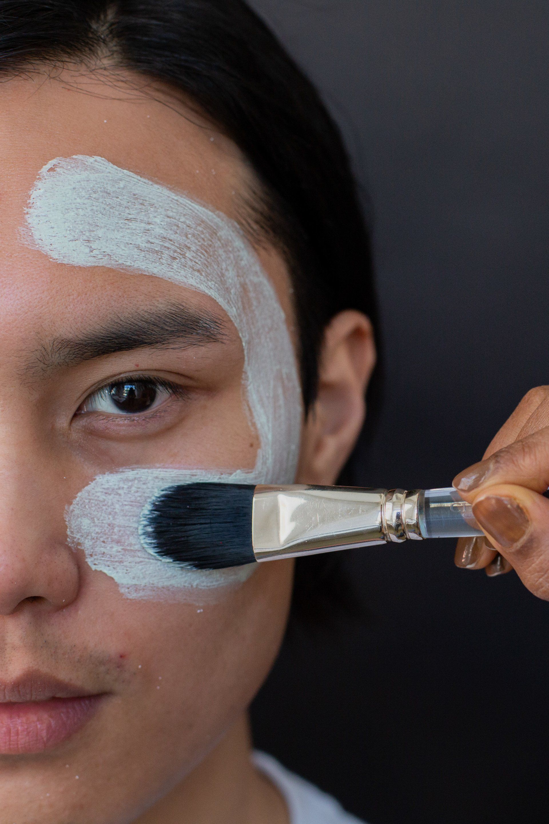 A Man Is Applying A Mask To His Face With A Brush