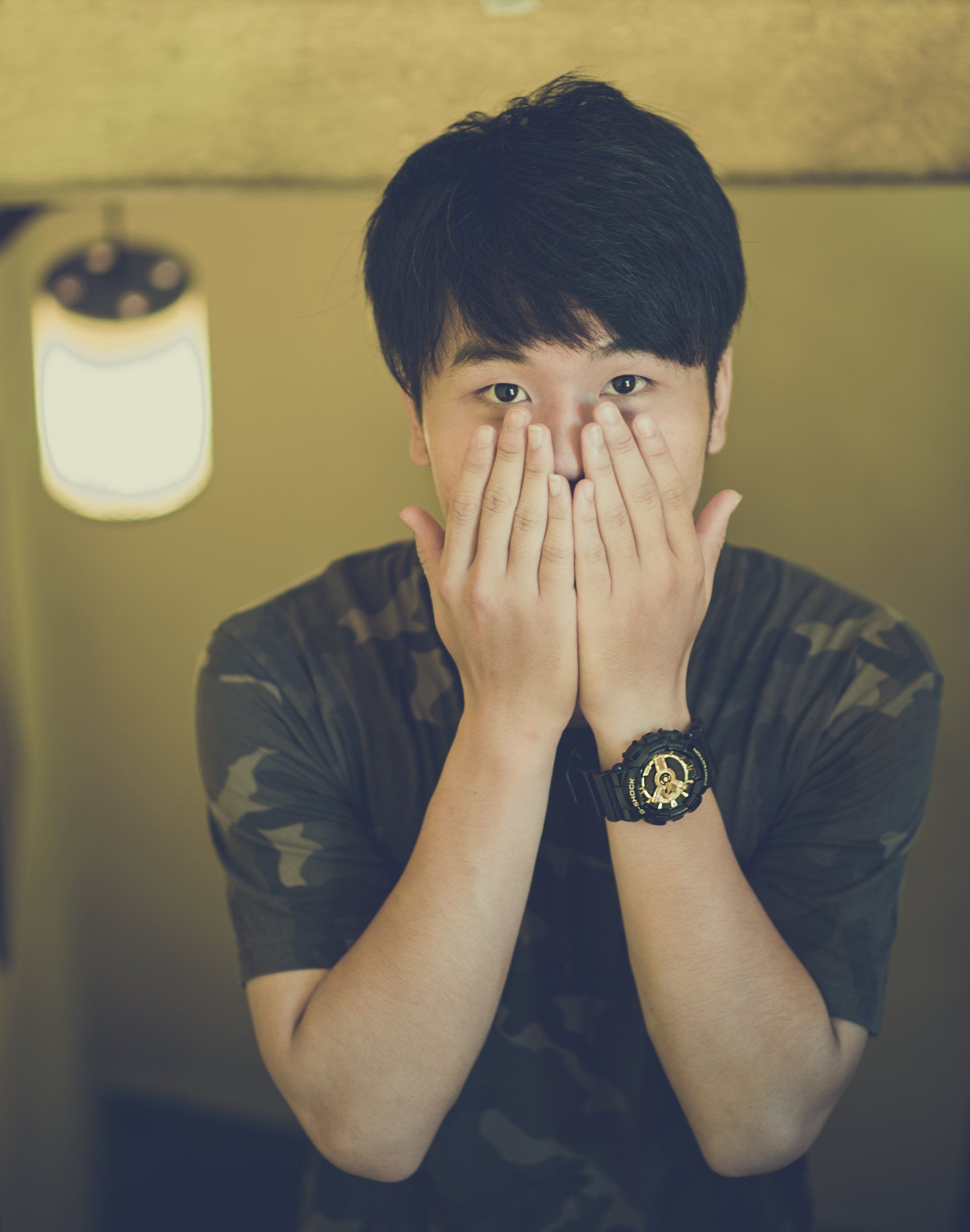 A man wearing a watch is covering his face with his hands