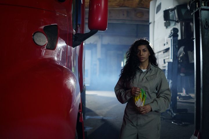 A woman is standing next to a red truck in a garage.