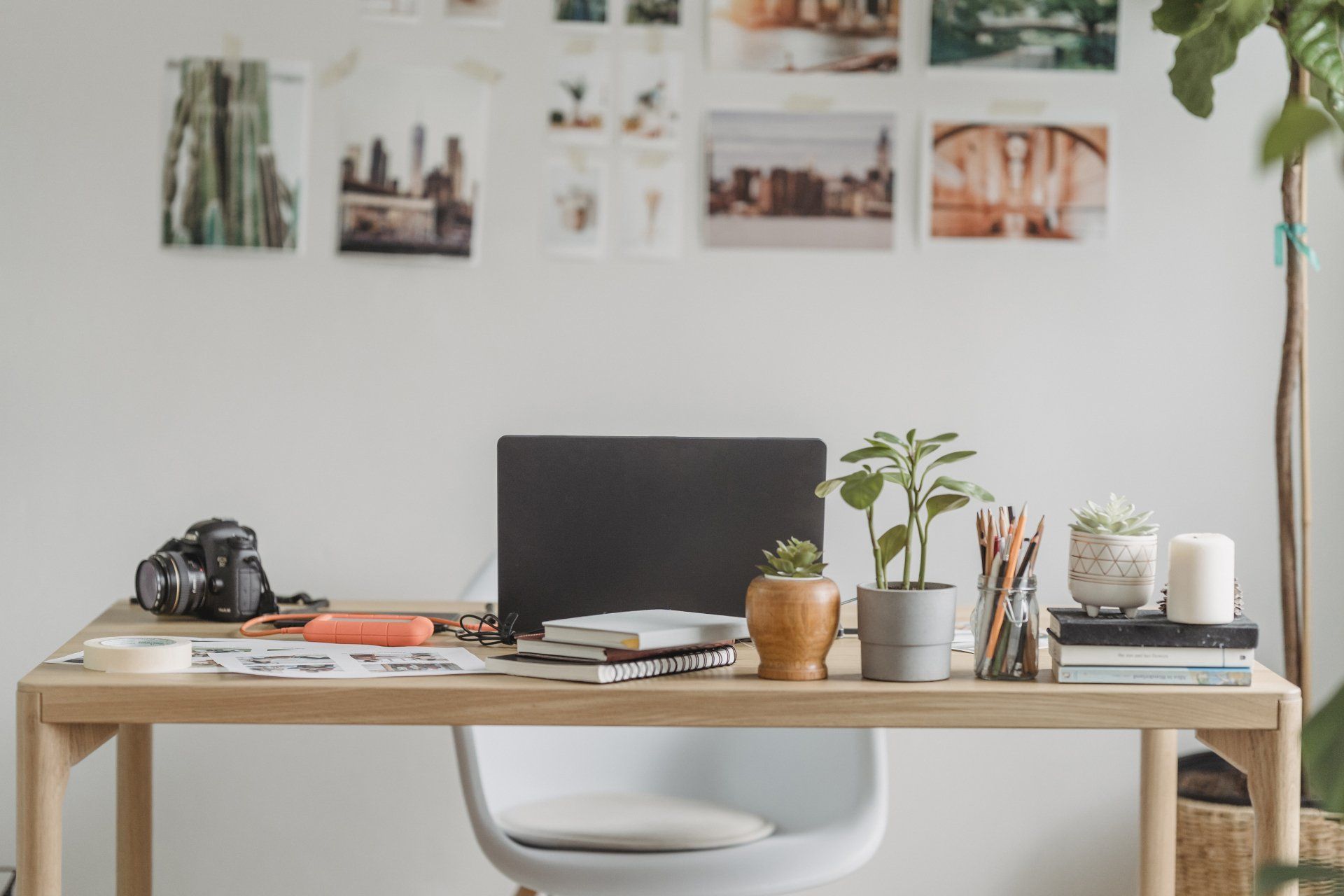 A wooden desk with a laptop , camera , and potted plants on it.