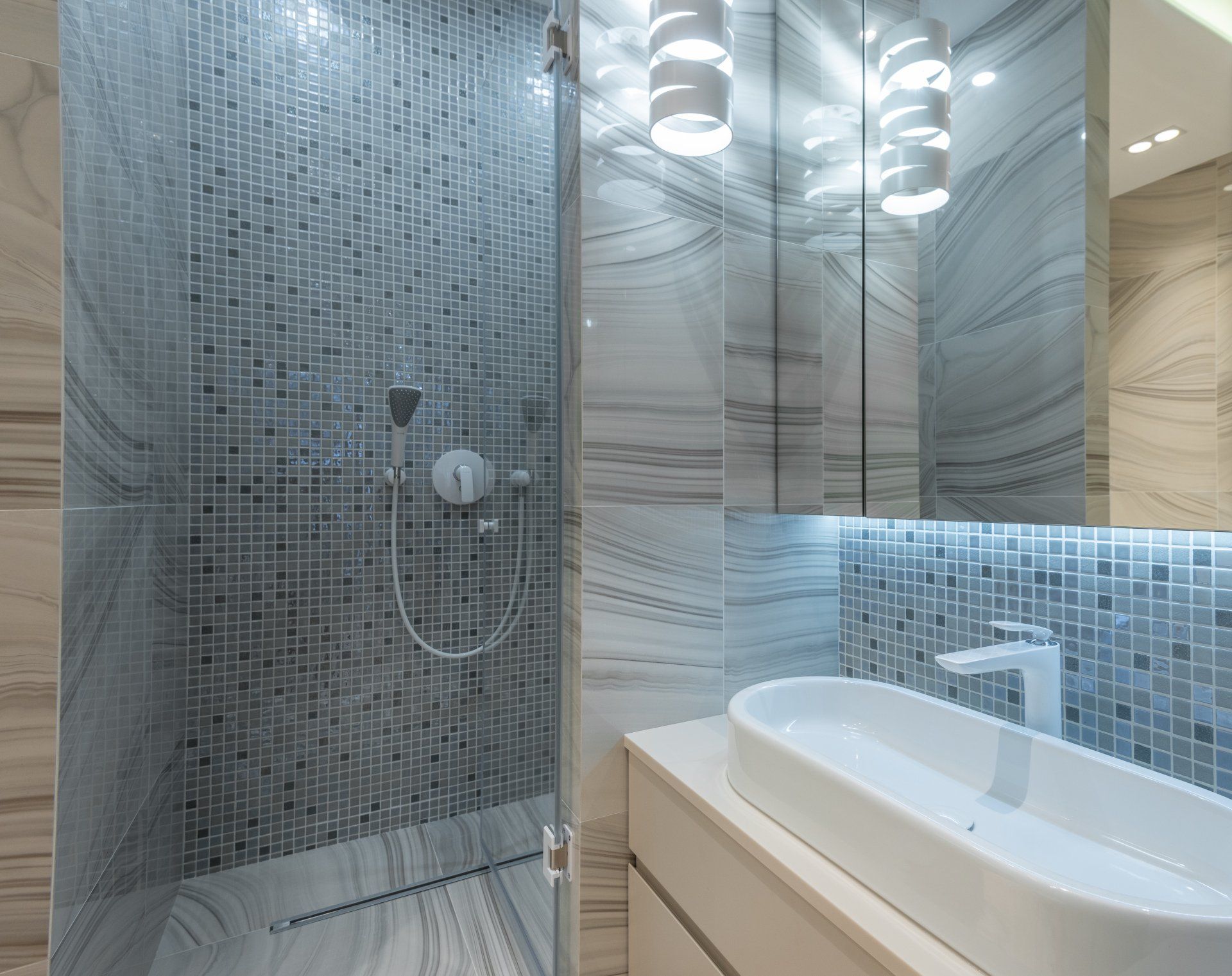 Modern bathroom with a glass shower, mosaic tile, marble walls, and a white vessel sink.