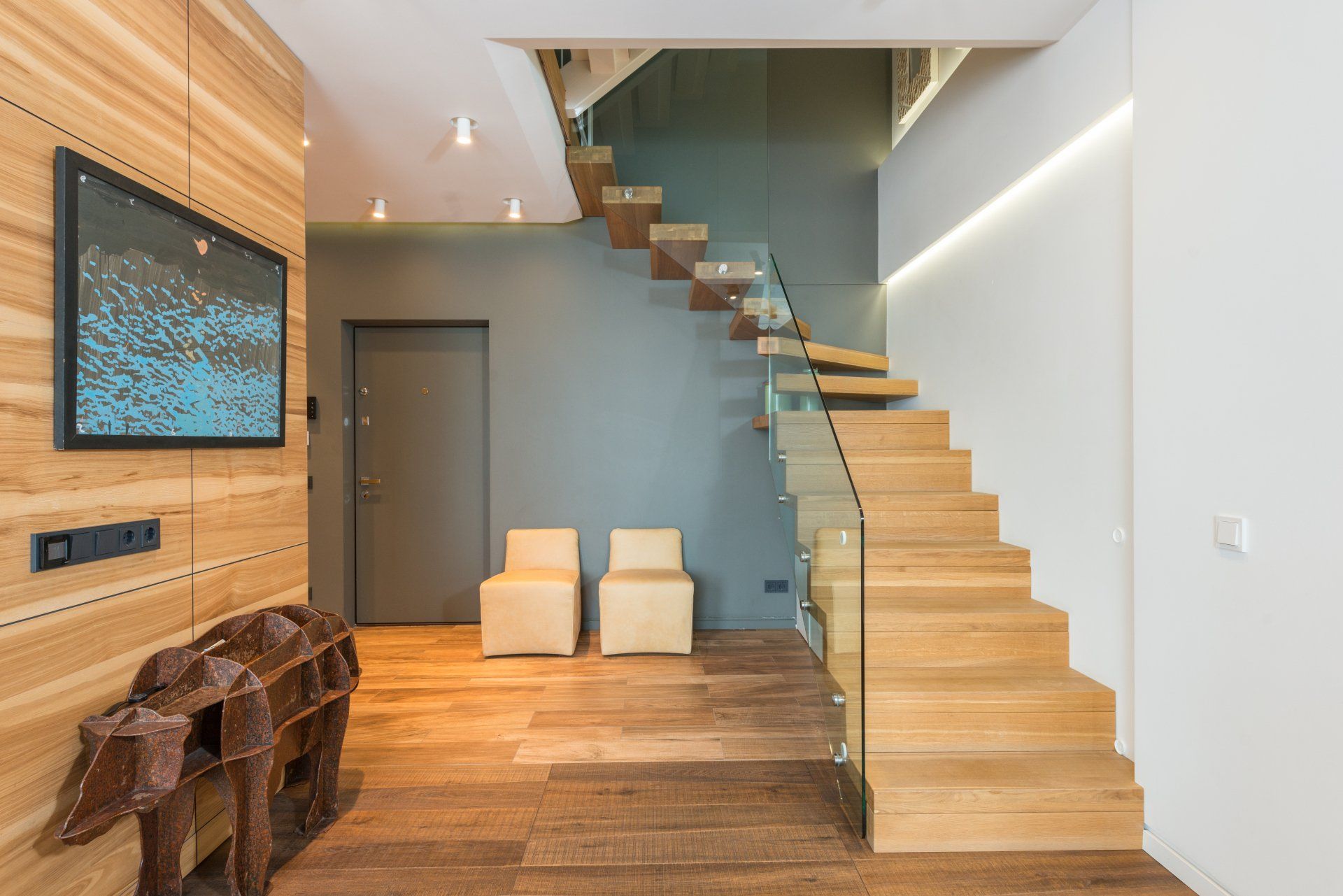 A wooden staircase with a glass railing and a flat screen tv on the wall.