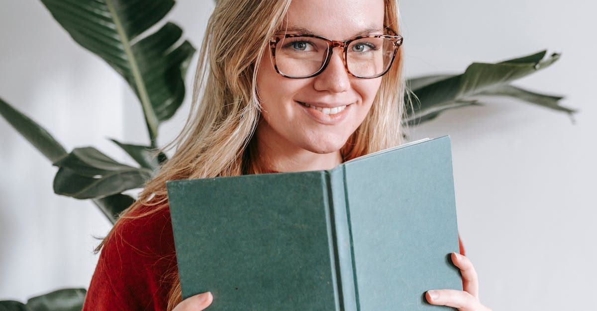 A smiling girl wearing glasses and holding an open book.
