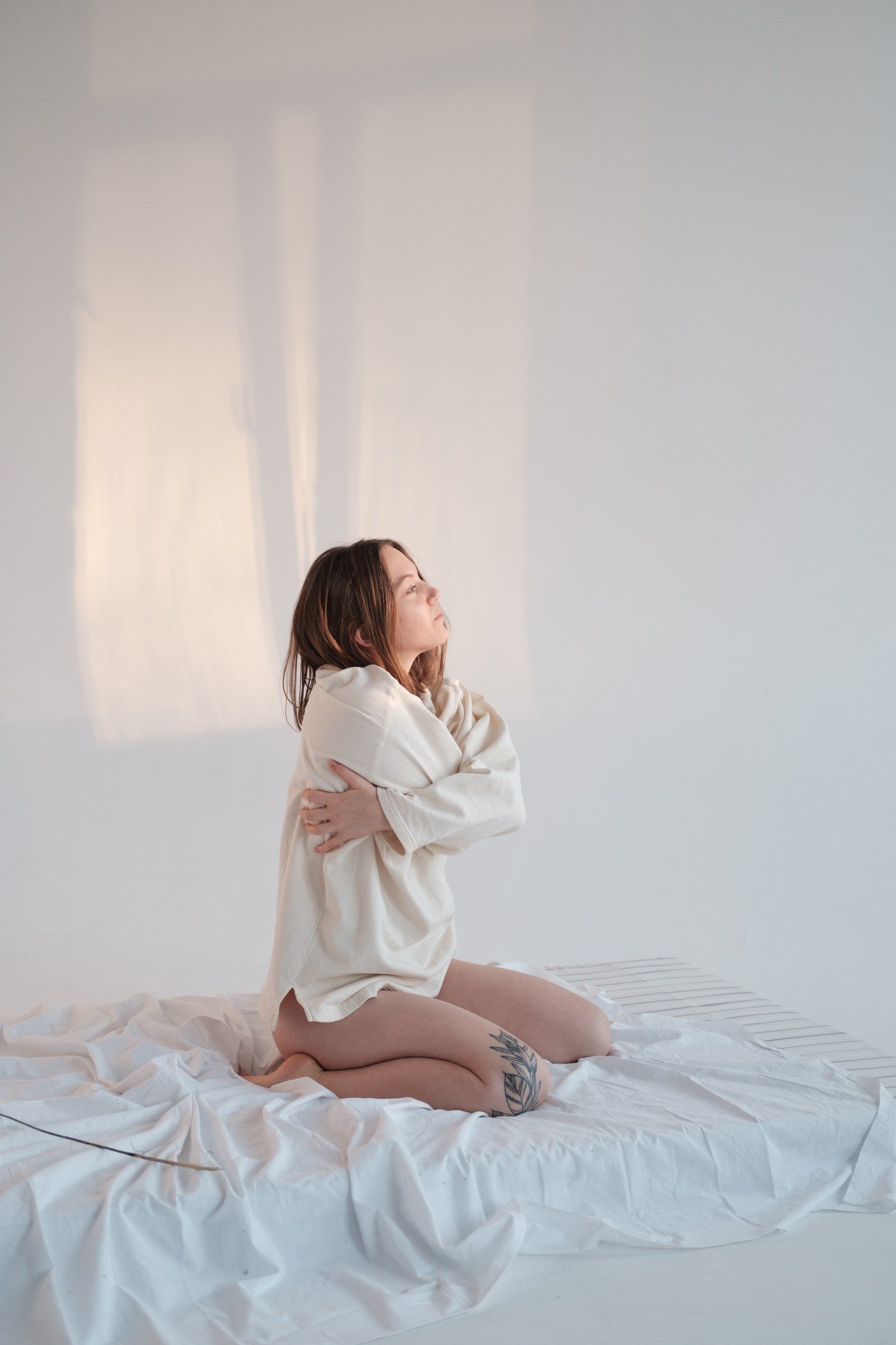 A woman is sitting on a bed hugging herself.