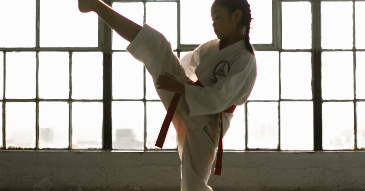 A young girl is practicing karate in front of a window.