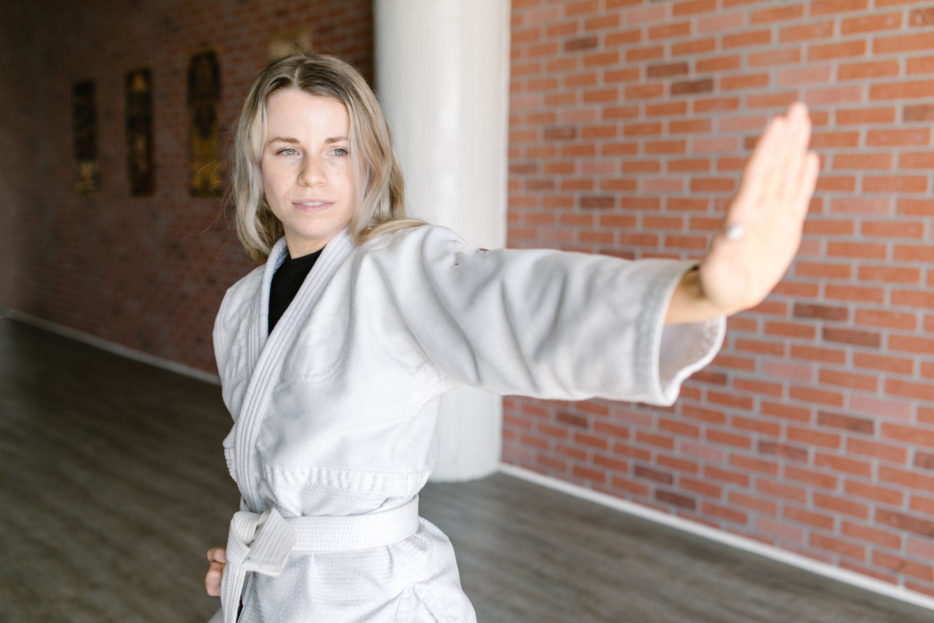 A woman in a white karate uniform is standing in front of a brick wall.
