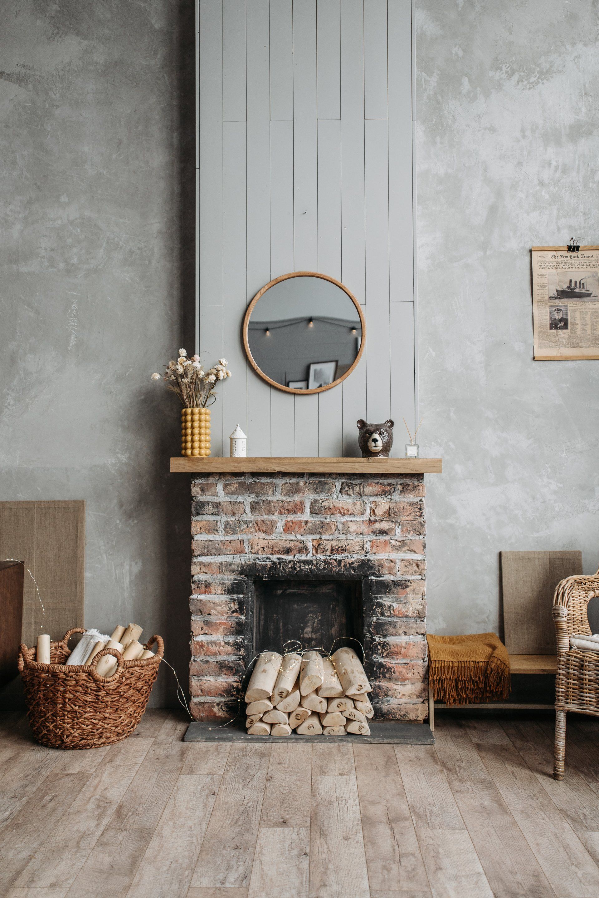 Fireplace with brick, logs, a round mirror, and a basket of firewood.